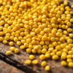 Fresh yellow mustard seeds being poured onto a wooden surface to showcase quality and authenticity